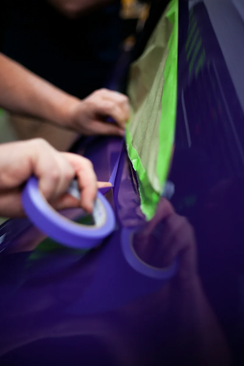 Detailer applying paint protection film with precision tools to protect a vehicle paint surface.