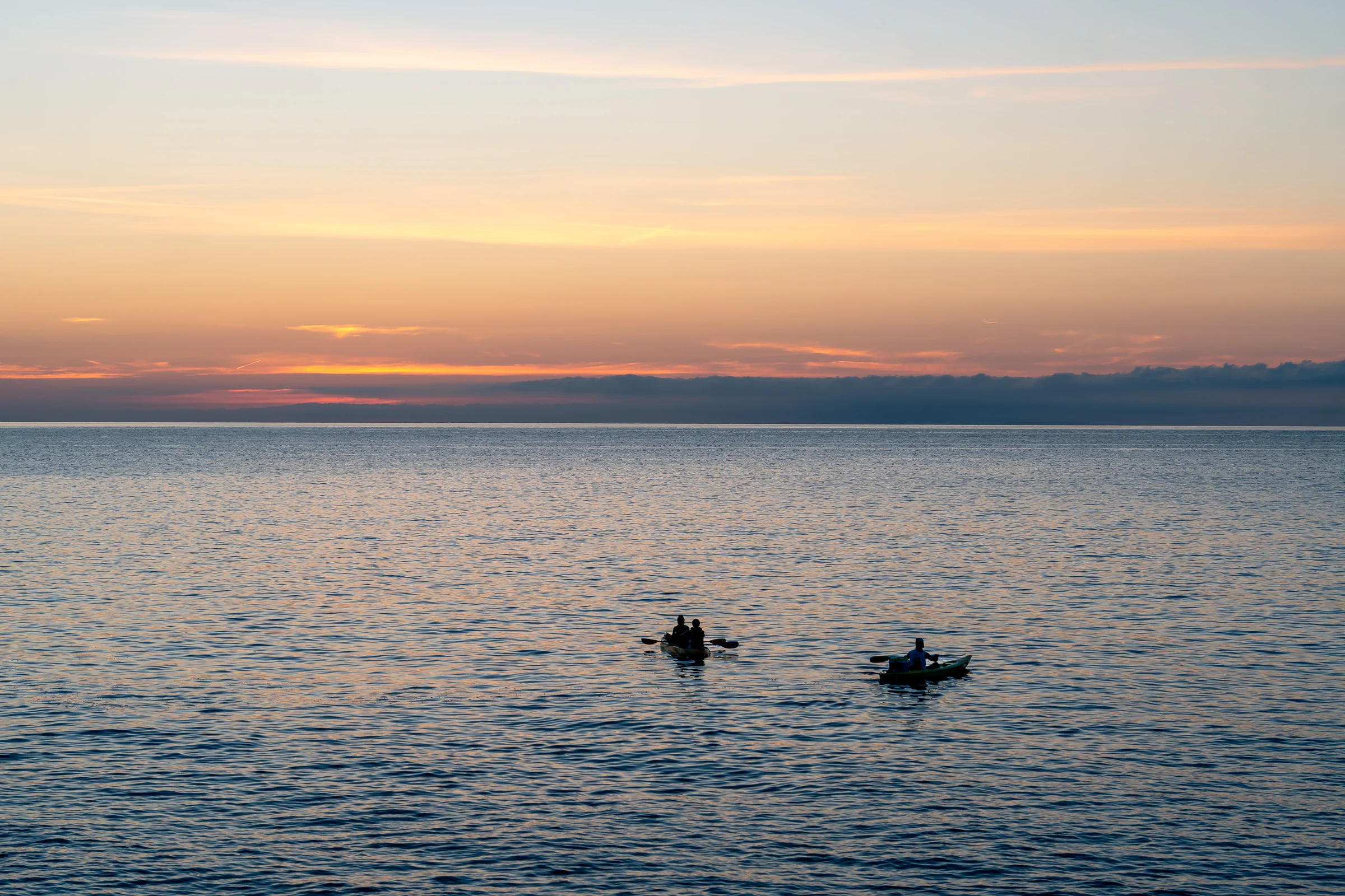 Kayakers silhouetted on the sea at sunrise