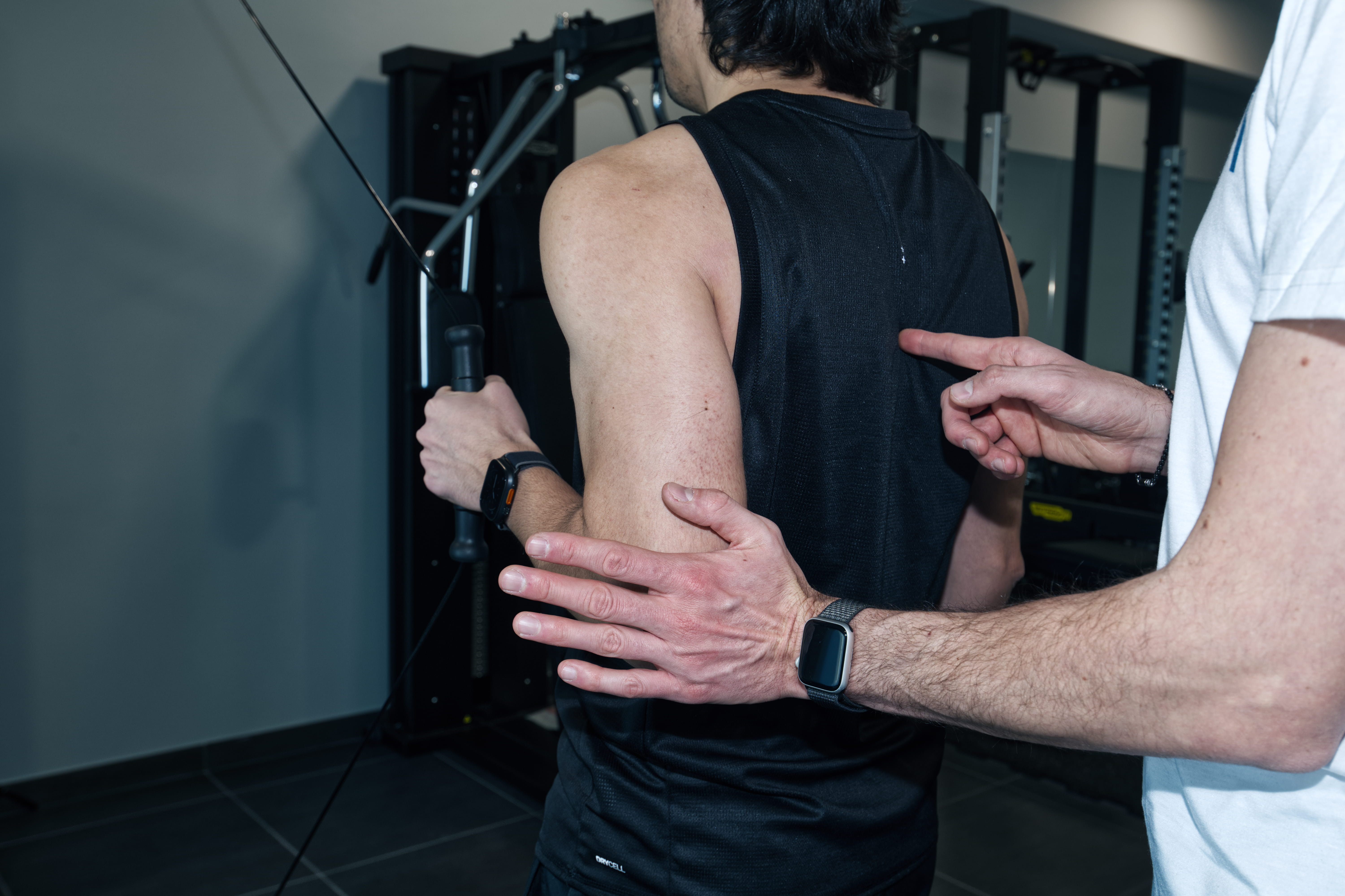 A person sits at a cluttered desk in a dimly lit room, focused on two monitors displaying aerial maps. The walls are covered with various images and notes.