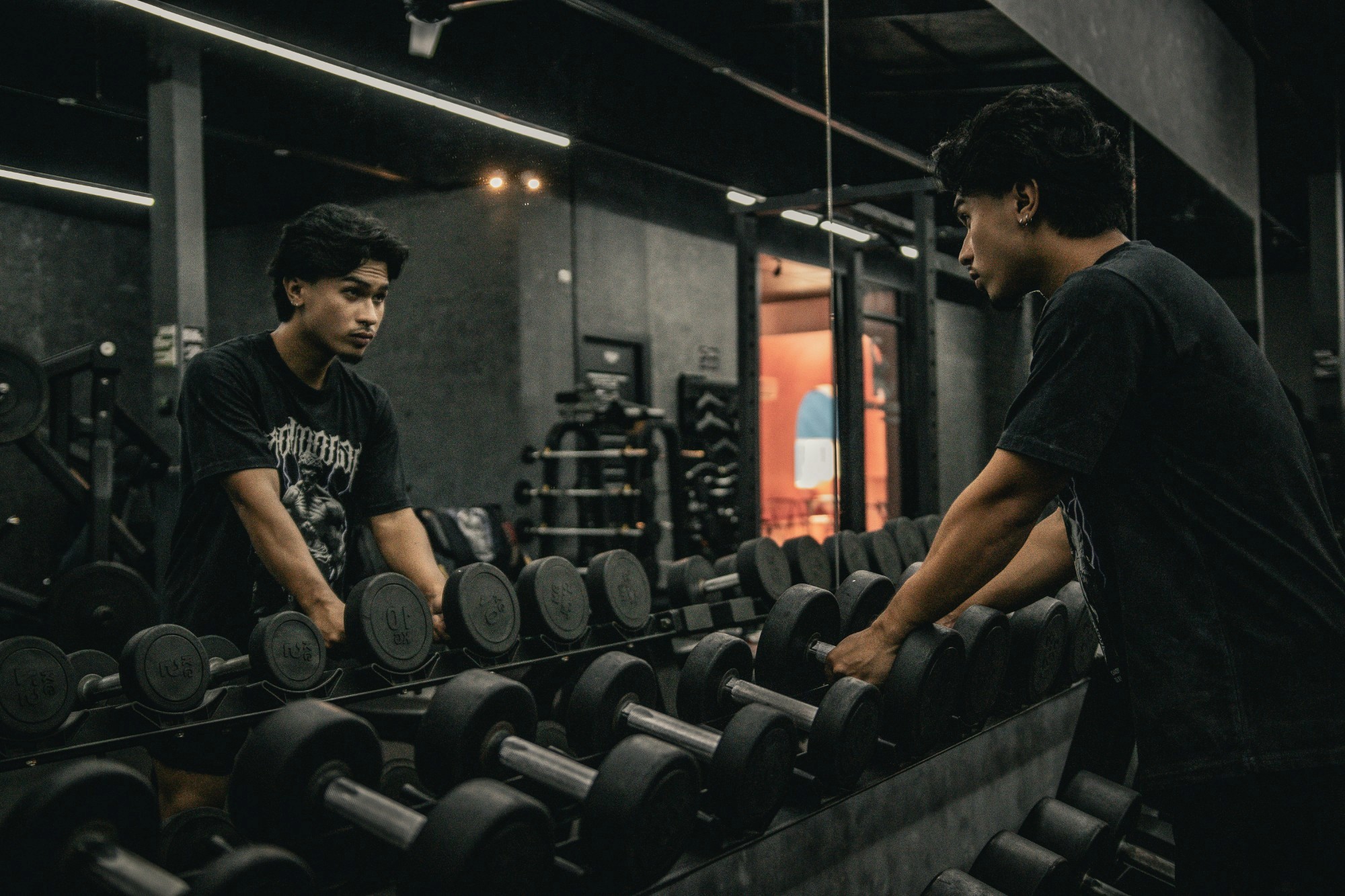 Two individuals are working out in a gym, focusing on dumbbells and strength training equipment.