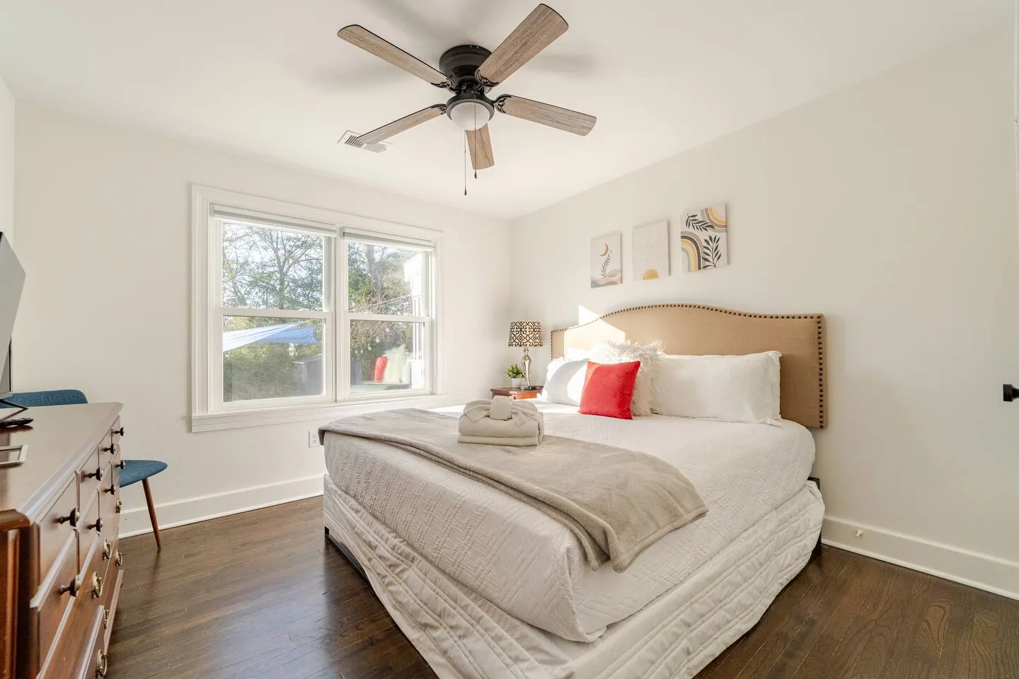 King bedroom with a tan upholstered headboard and a wood dresser