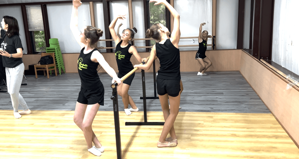 Girls doing ballet class with ballet teacher overseeing their movements from the side