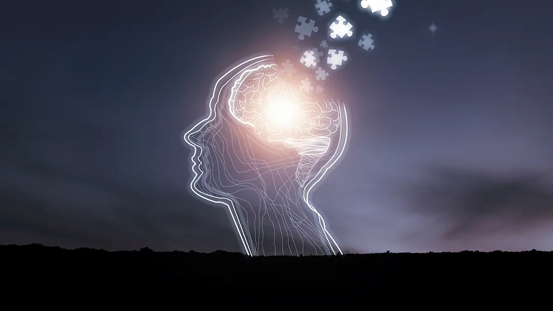 Glowing outline of a human head against a night sky, a lit brain inside, with puzzle pieces drifting away from it.