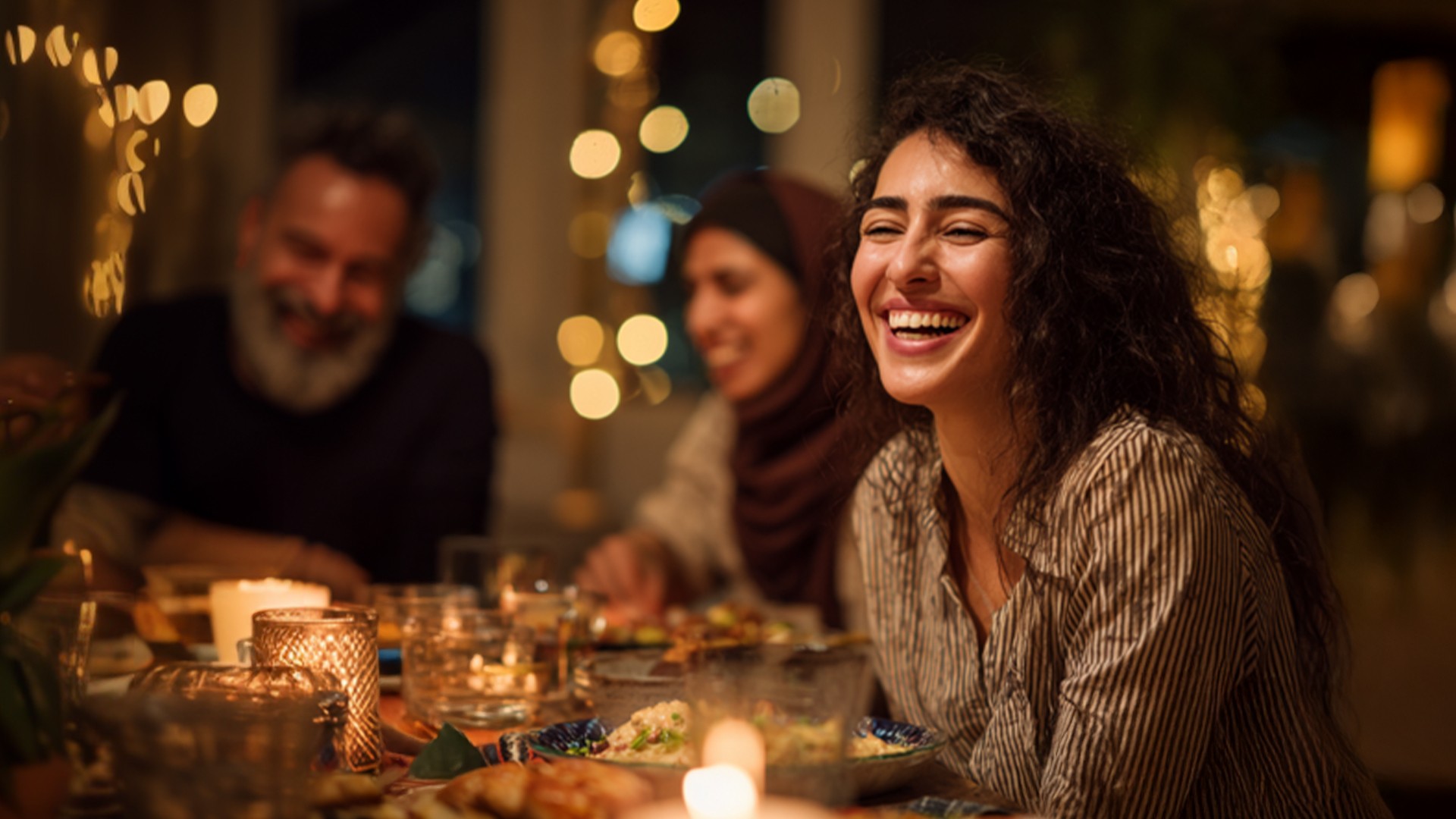Fröhliche Menschen sitzen abends bei warmem Kerzenlicht gemeinsam am Tisch und brechen das Fasten, natürliche Gesichtsausdrücke und harmonische Atmosphäre, Symbol für Gemeinschaft und Ramadan
