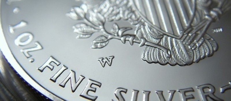A young person with curly hair smiles at the camera while sitting in front of a laptop against a dark background.
