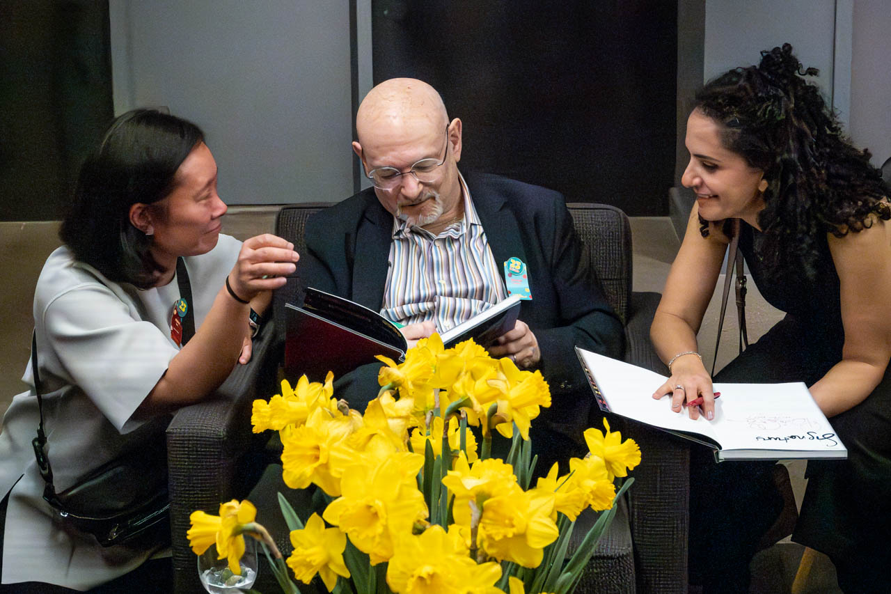 Three people signing books, sitting on a couch