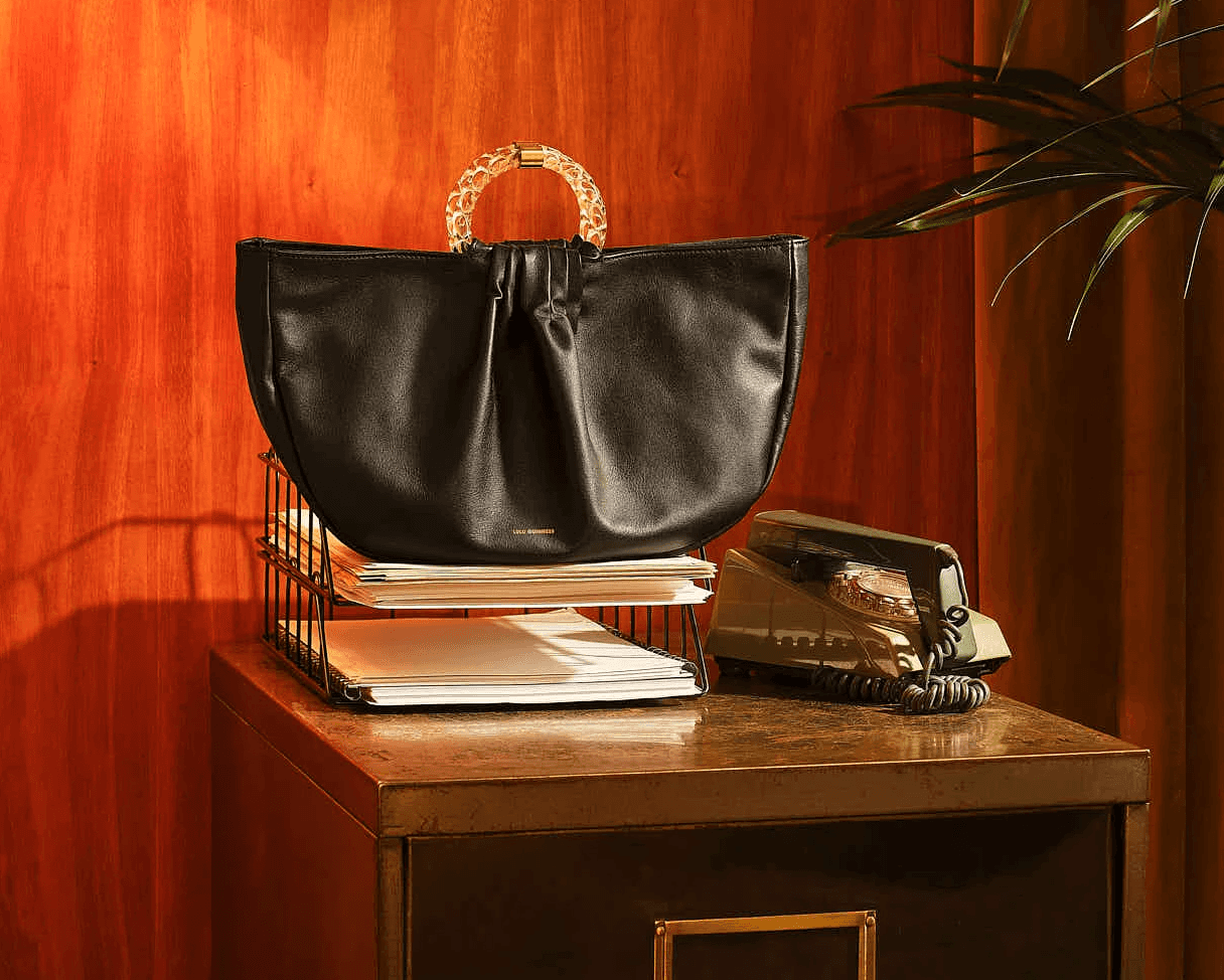 Vintage leather handbag with rattan handles on a retro office desk with papers and rotary phone.
