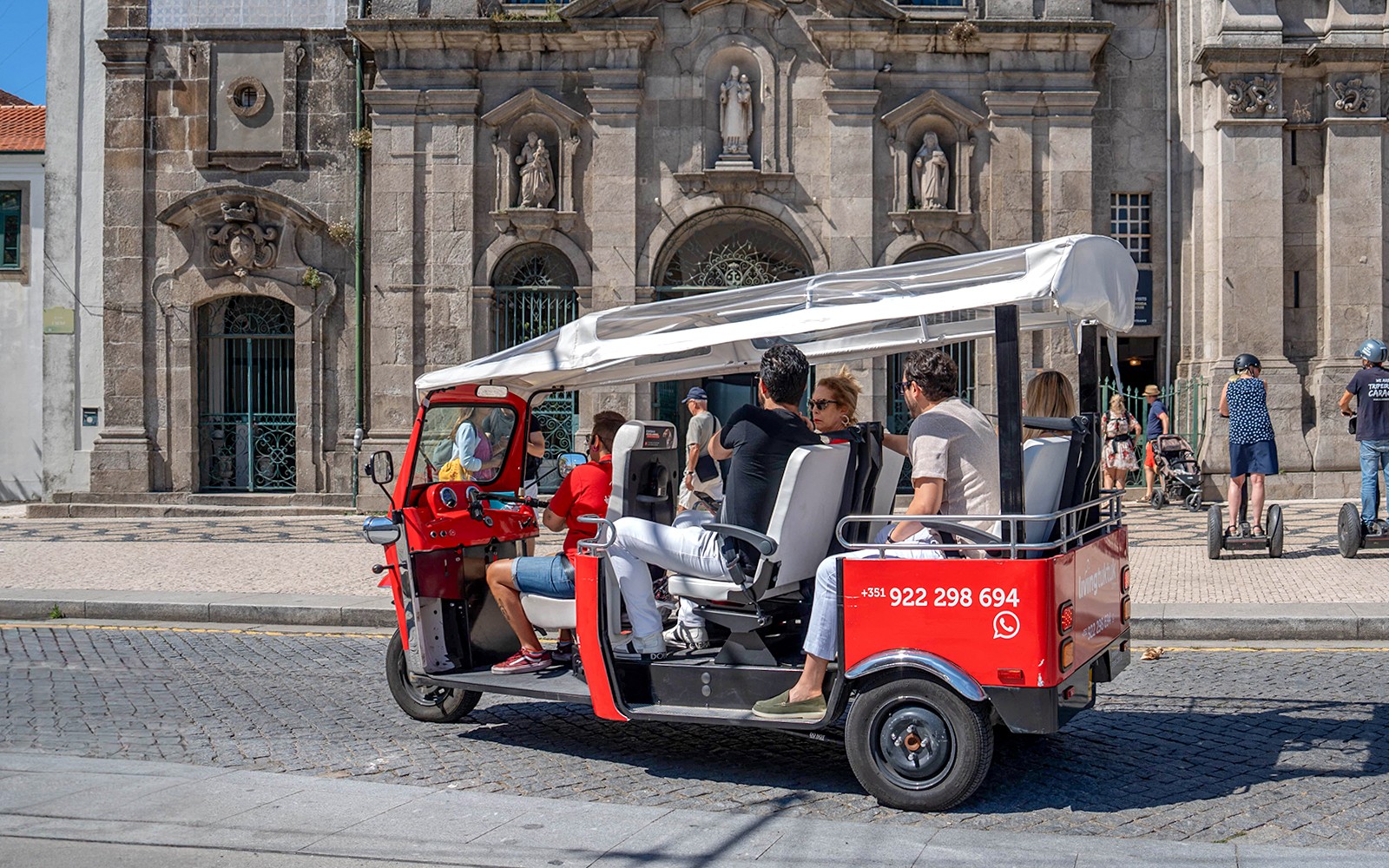 Tuk-tuk eléctrico en Oporto con turistas frente a un edificio histórico.