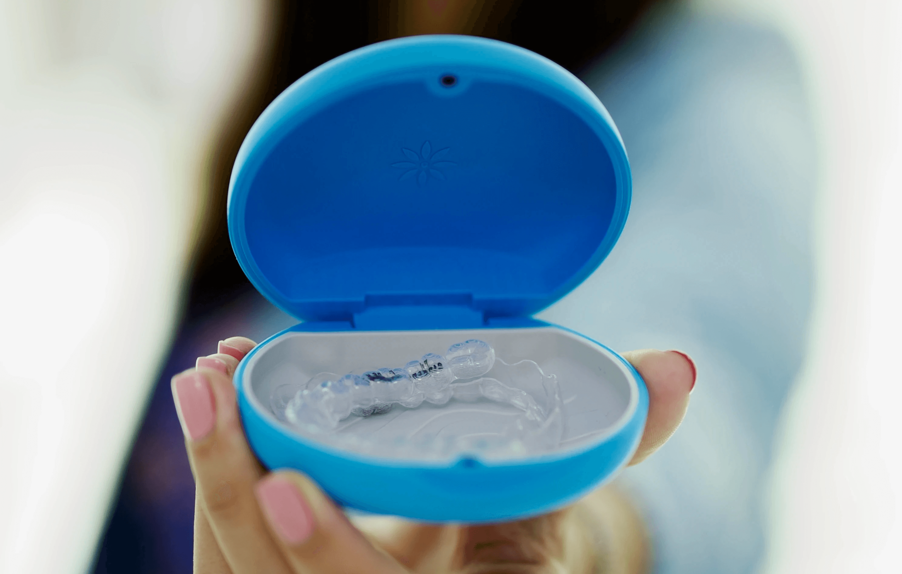 Clear dental aligner in open blue case held by hand.