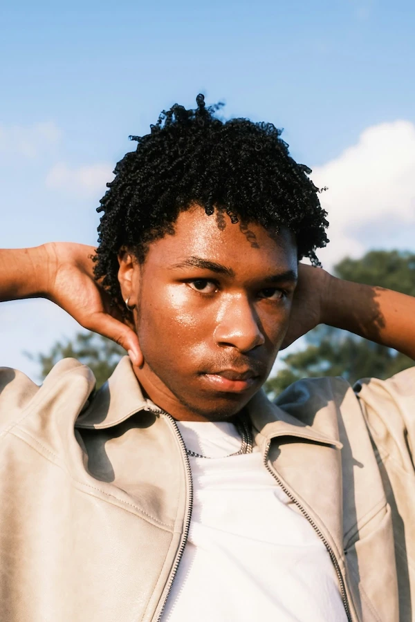 black-skinned man with dreadlocks, jacket and white T-shirt underneath, photo taken outdoors