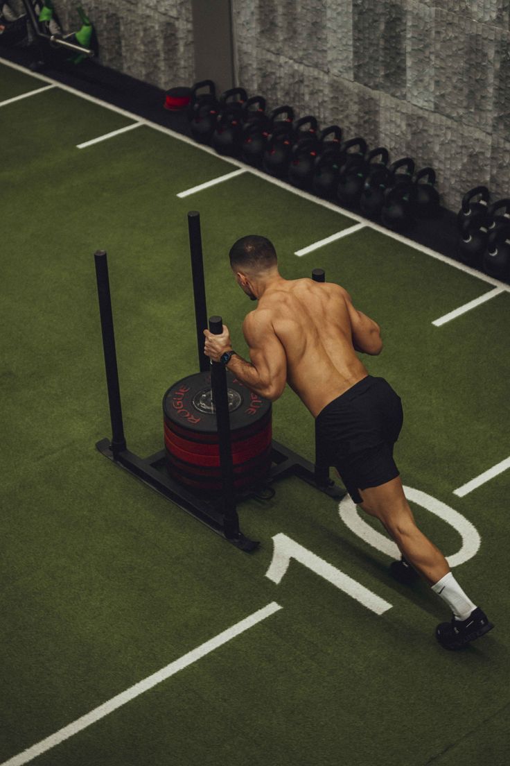Man pushing a weighted sled on gym turf.