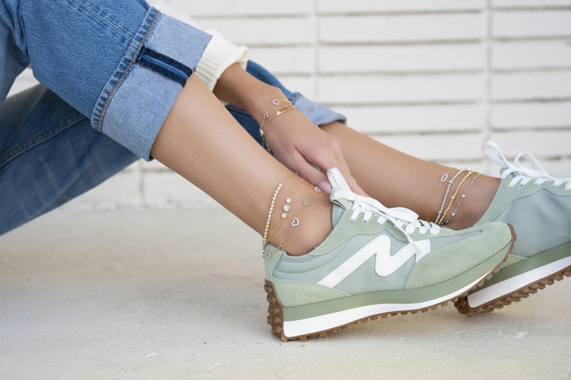 photography of anklets featured on a models ankles, while she's wearing blue jean capris and green tennis shoes.