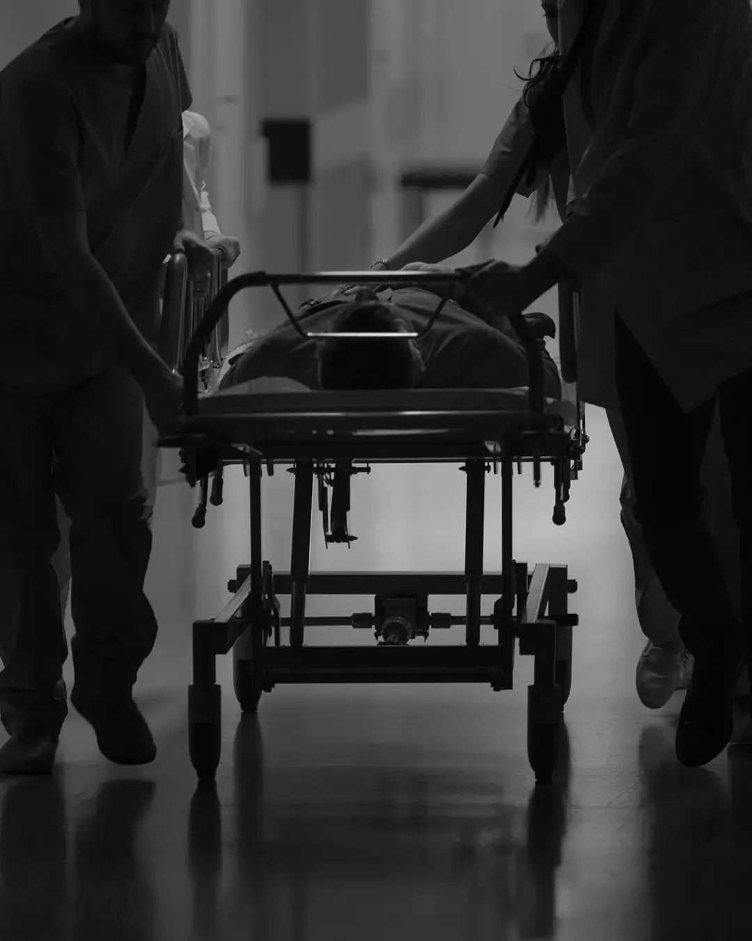 Medical staff swiftly wheel a patient on a stretcher through a dimly lit hospital corridor, with the silhouette highlighting the urgency and intensity of an emergency situation.