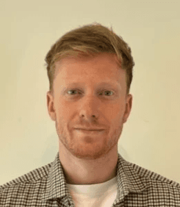 A woman with short curly hair wearing a black t-shirt looks into the camera.