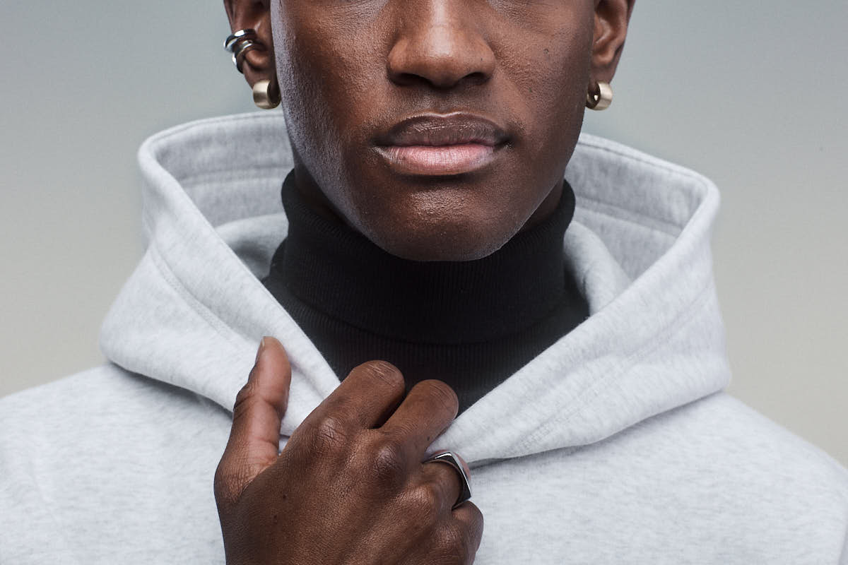 Close-up of a person wearing a black turtle neck and light grey Sunday Superior Hoodie