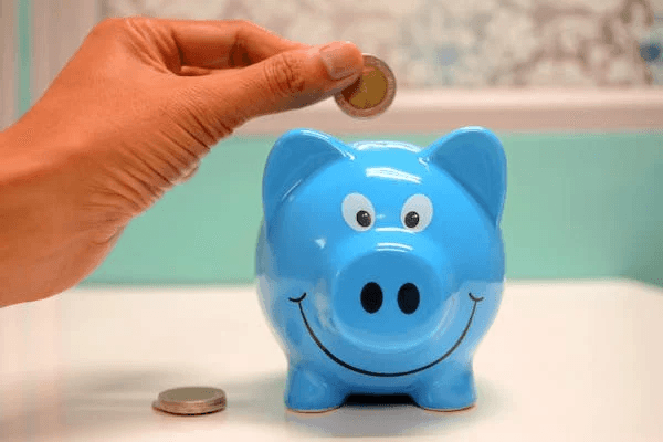 A hand depositing a coin into a blue piggy bank, symbolizing saving money for a US bank account.