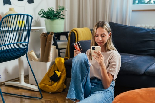 A person sitting on the floor with a guitar, casually smiling in a cozy living room setting.