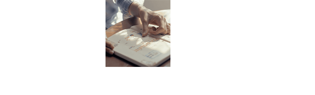 Close-up of hands writing or sketching in an open notebook on a wooden surface in natural lighting