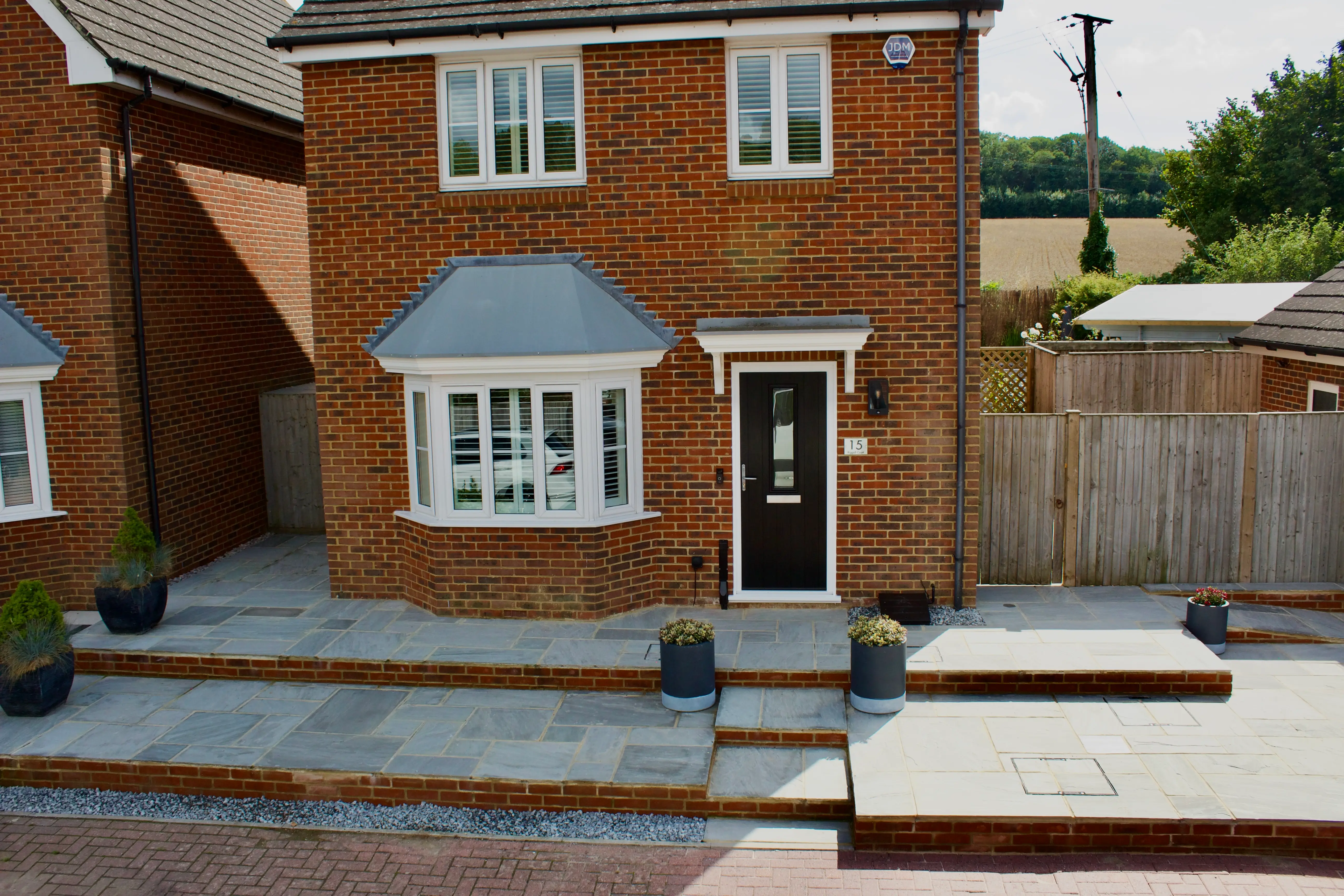 A two-story brick house with white windows and a black front door, surrounded by a stone pathway and garden area.