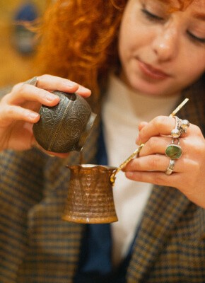 A woman pouring Turkish coffee from a cezve (copper pot) in a workshop, illustrating the traditional method of coffee preparation in Istanbul.