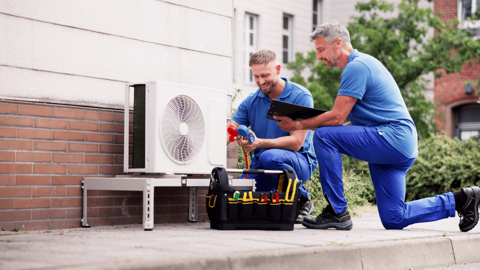 Two HVAC engineers servicing an outdoor heat pump unit, performing diagnostic checks and maintenance work on a residential property.