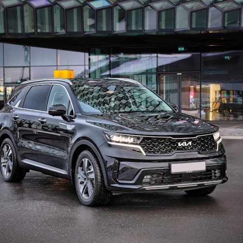 SUV negra estacionada en un pavimento mojado frente a un edificio moderno de cristal con patrones geométricos.