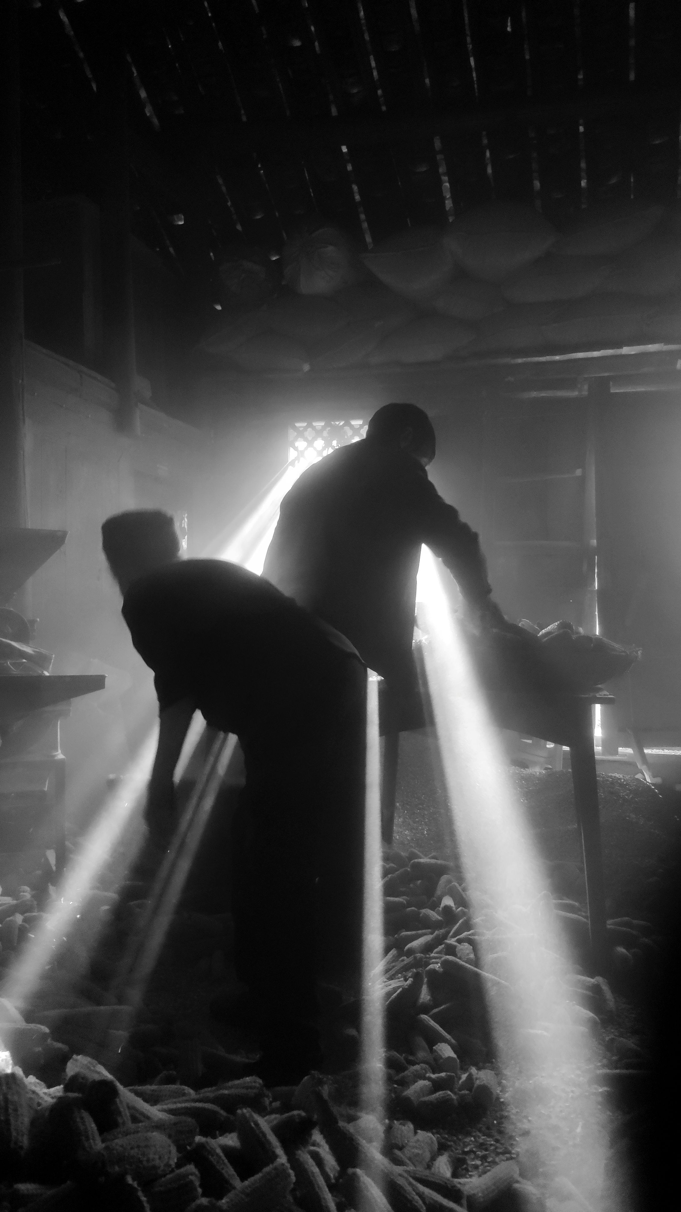 Two men at work in an old workshop, lit by beams of light