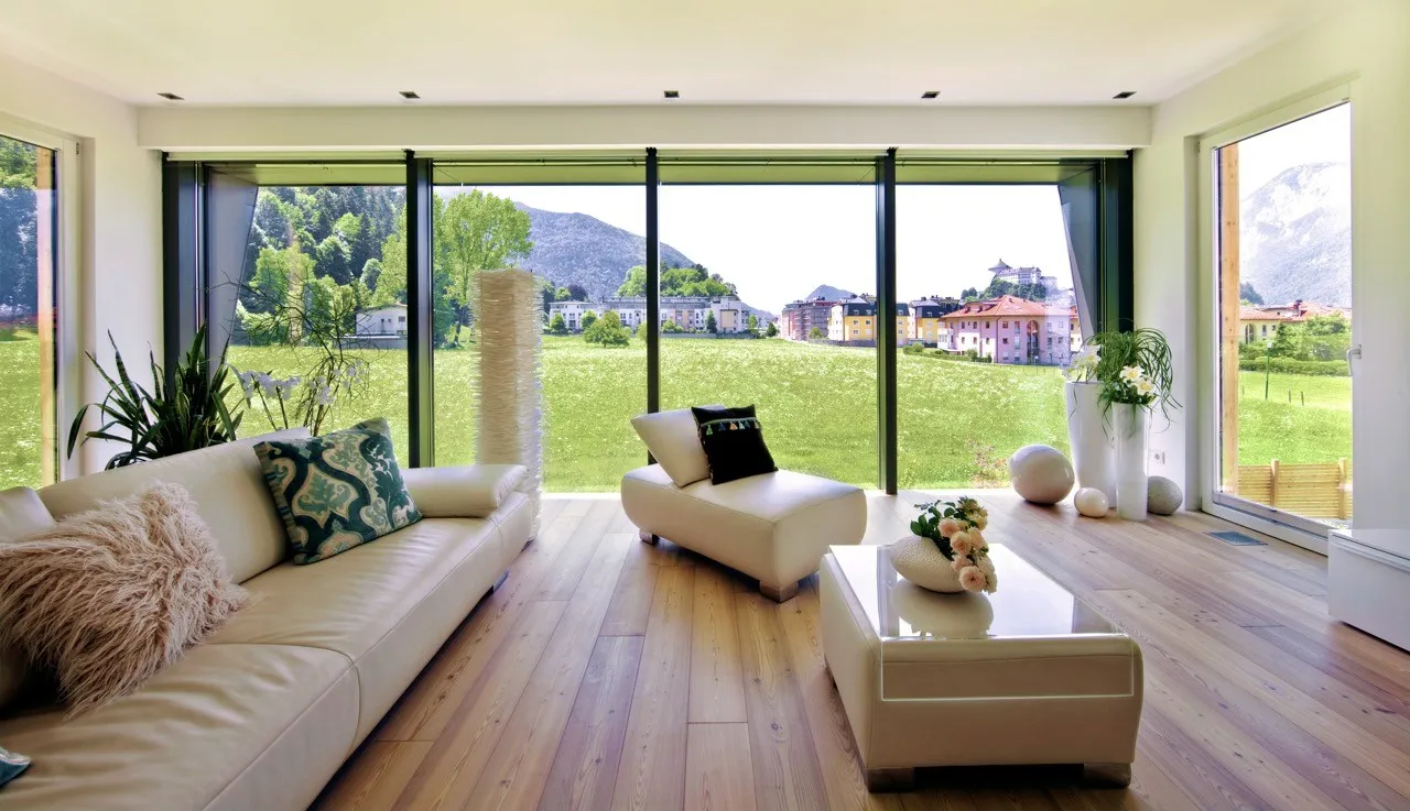 Modernes Wohnzimmer mit Ledermöbeln und Panoramafenstern, die auf eine grüne Landschaft und Berge blicken.