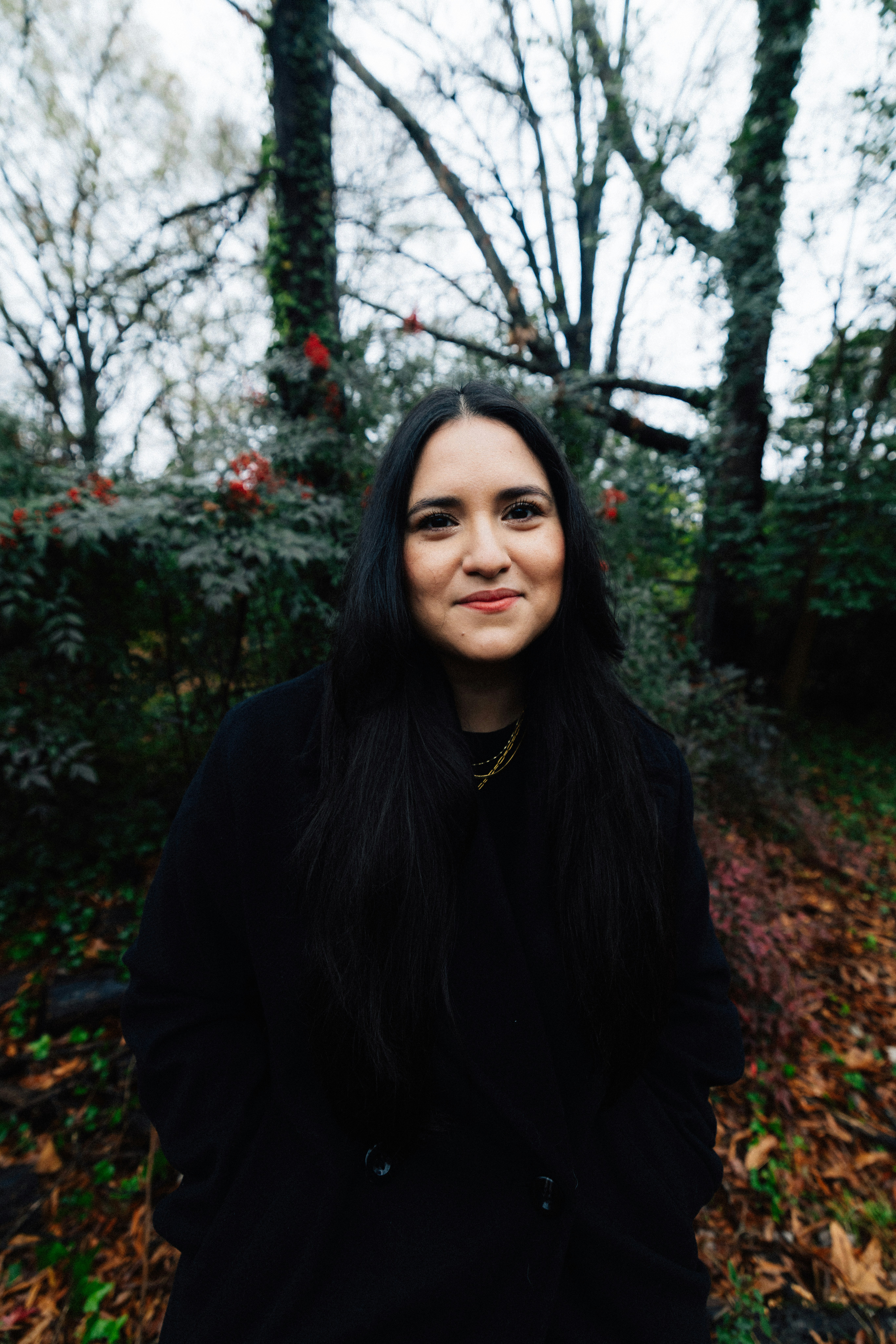 A woman with long dark hair smiles outdoors.