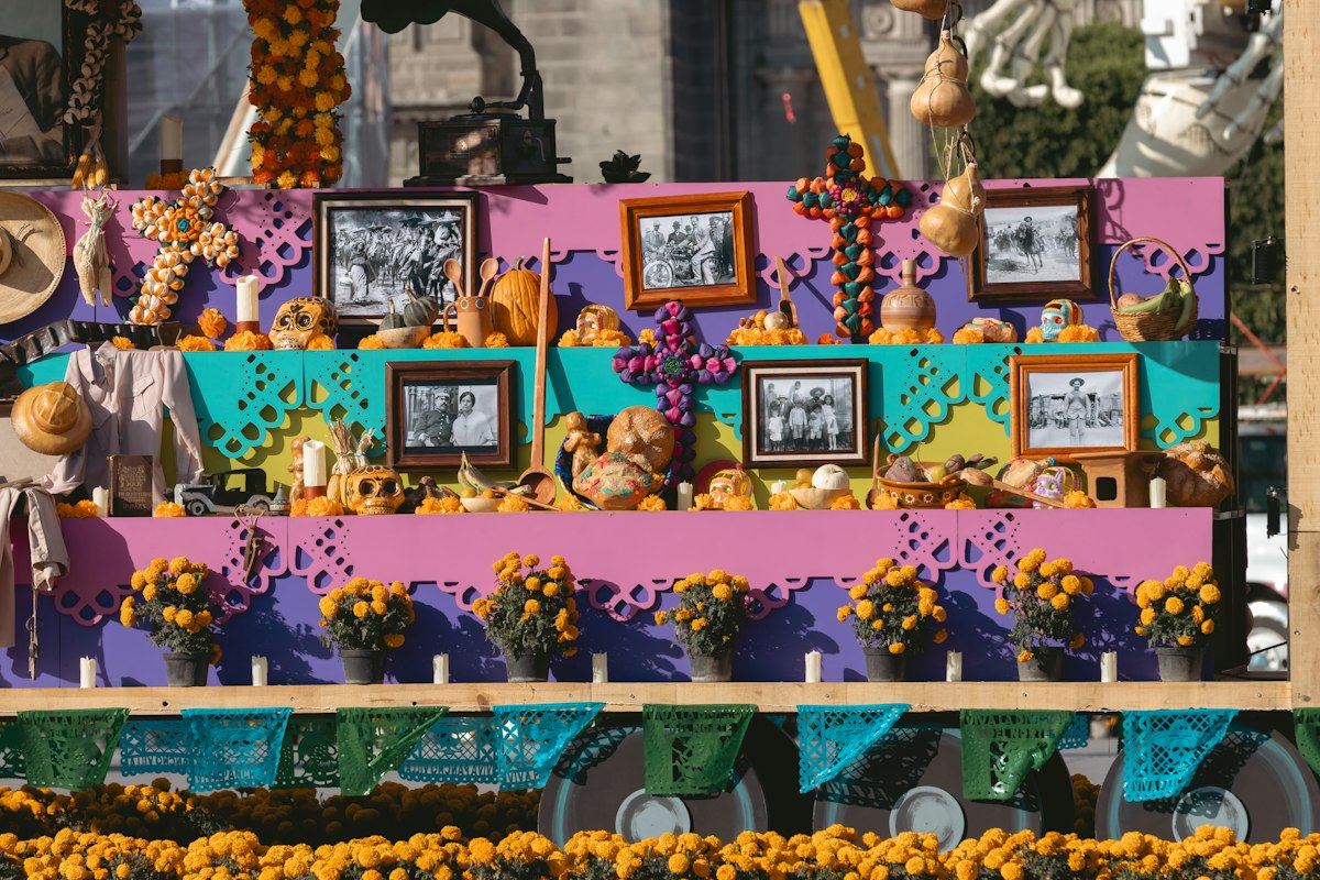 Public ofrenda lined with framed family portraits, potted marigolds, candles and cut papel picado
