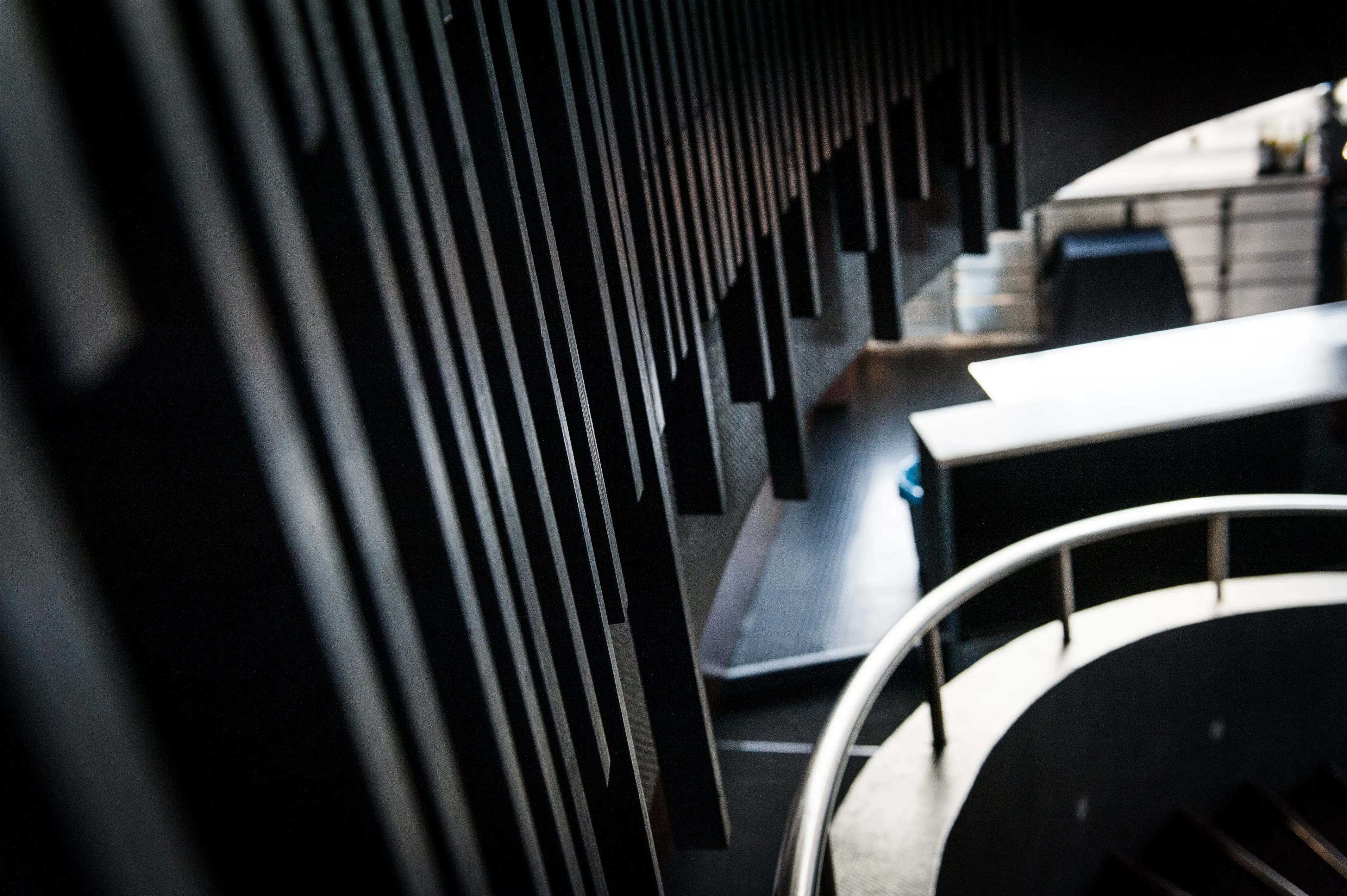 Architectural detail at SOLAR SKY LOUNGE with dark vertical wooden slats casting long shadows and a curved white railing of the staircase below.