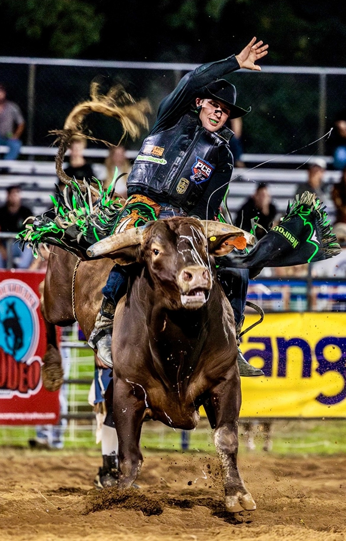 Professional bull rider Alex Goins riding a bucking bull while wearing protective gear and a black cowboy hat.