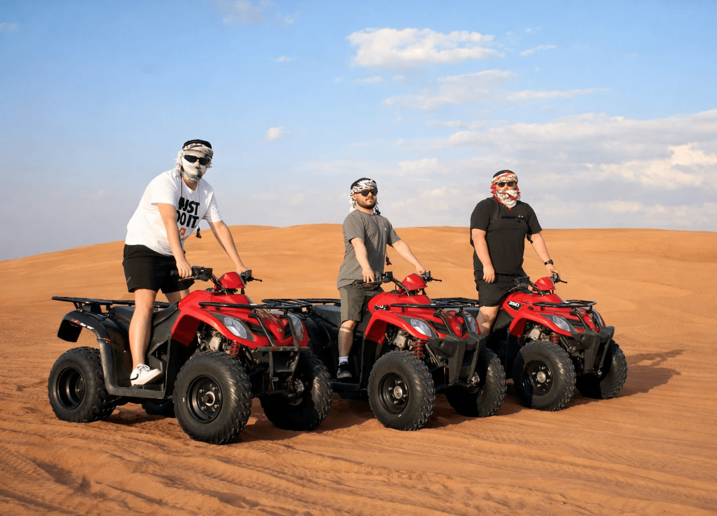 Group riding Kymco 250cc quad bikes across Dubai desert dunes during a quad biking adventure with Dune Quest Tours