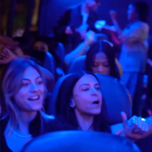 A group of people on a bus or train, illuminated by blue lighting, some appear to be talking and enjoying the ride.