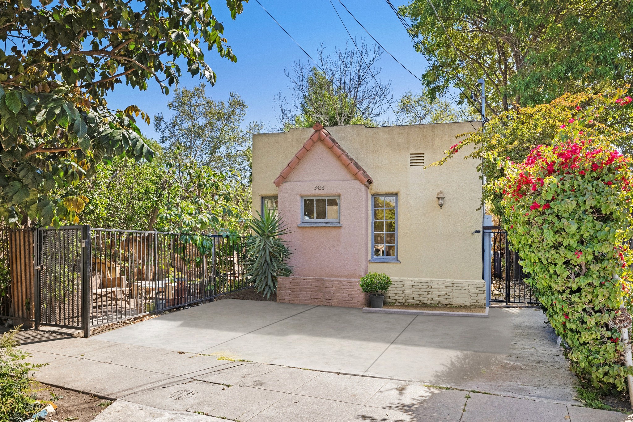 A quaint, pastel-colored fourplex at 3456 plata, surrounded by lush greenery and a concrete driveway.