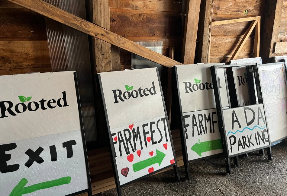 Hand-painted Rooted Northwest signs pointing toward Farm Fest, parking, and exits inside a barn.