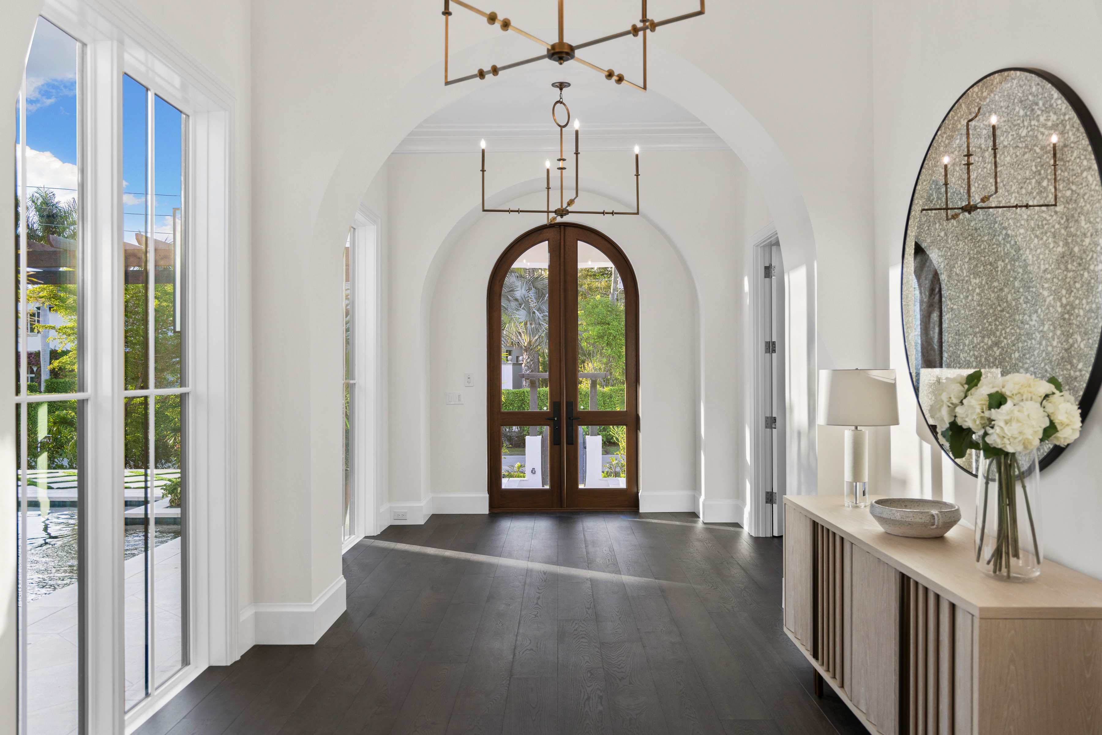 a modern entryway to a large home with a arched spruce door and windows lining the hallway