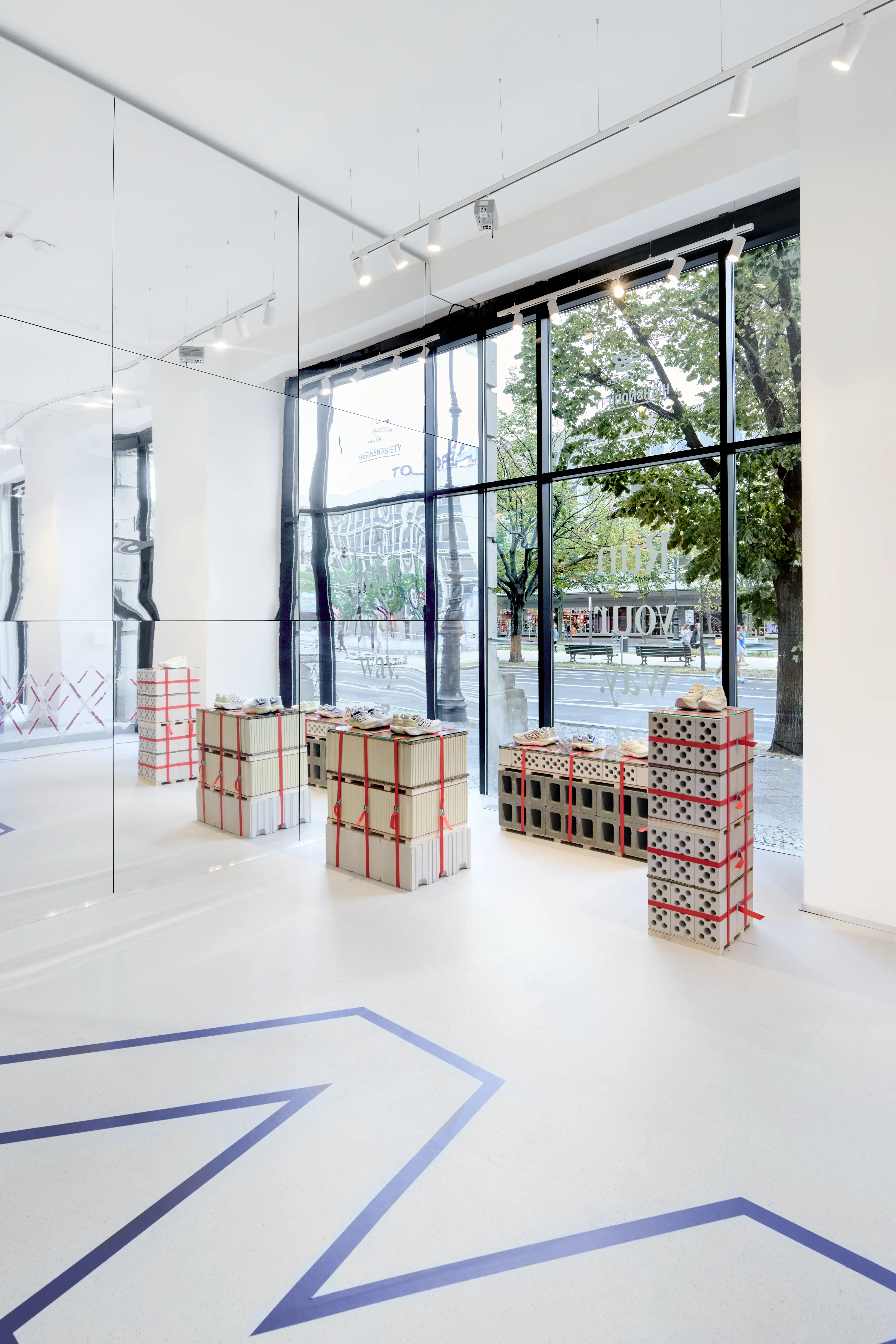 Sneaker displays on cinder-block plinths strapped with red bands in front of the glass facade of the Highsnobiety x New Balance pop-up.