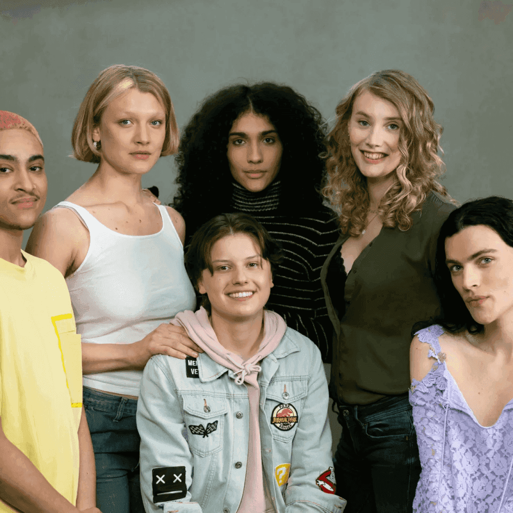 Een diverse groep van zes mensen poseert samen, glimlachend, voor een neutrale achtergrond.