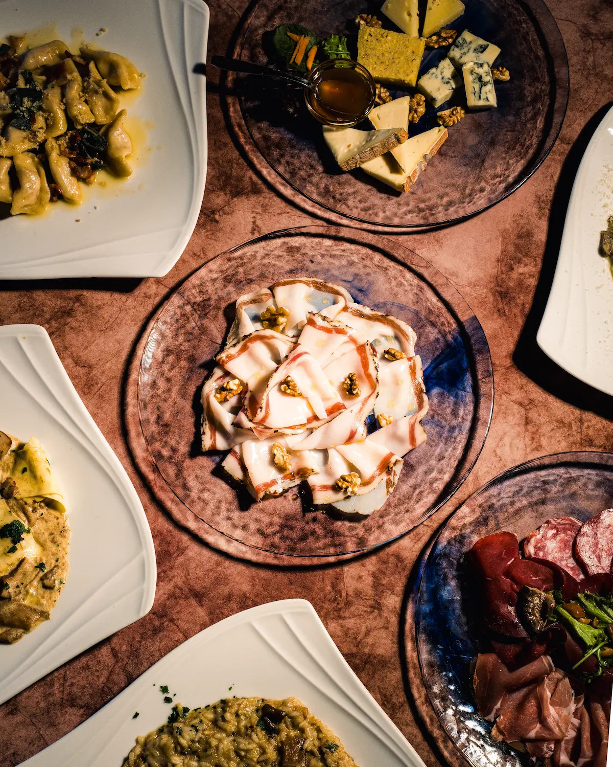A person in an apron uses a wooden peel to place a freshly baked loaf of artisan bread into a rustic, wood-fired oven, with a flickering fire visible inside, set against the backdrop of a sunlit kitchen.