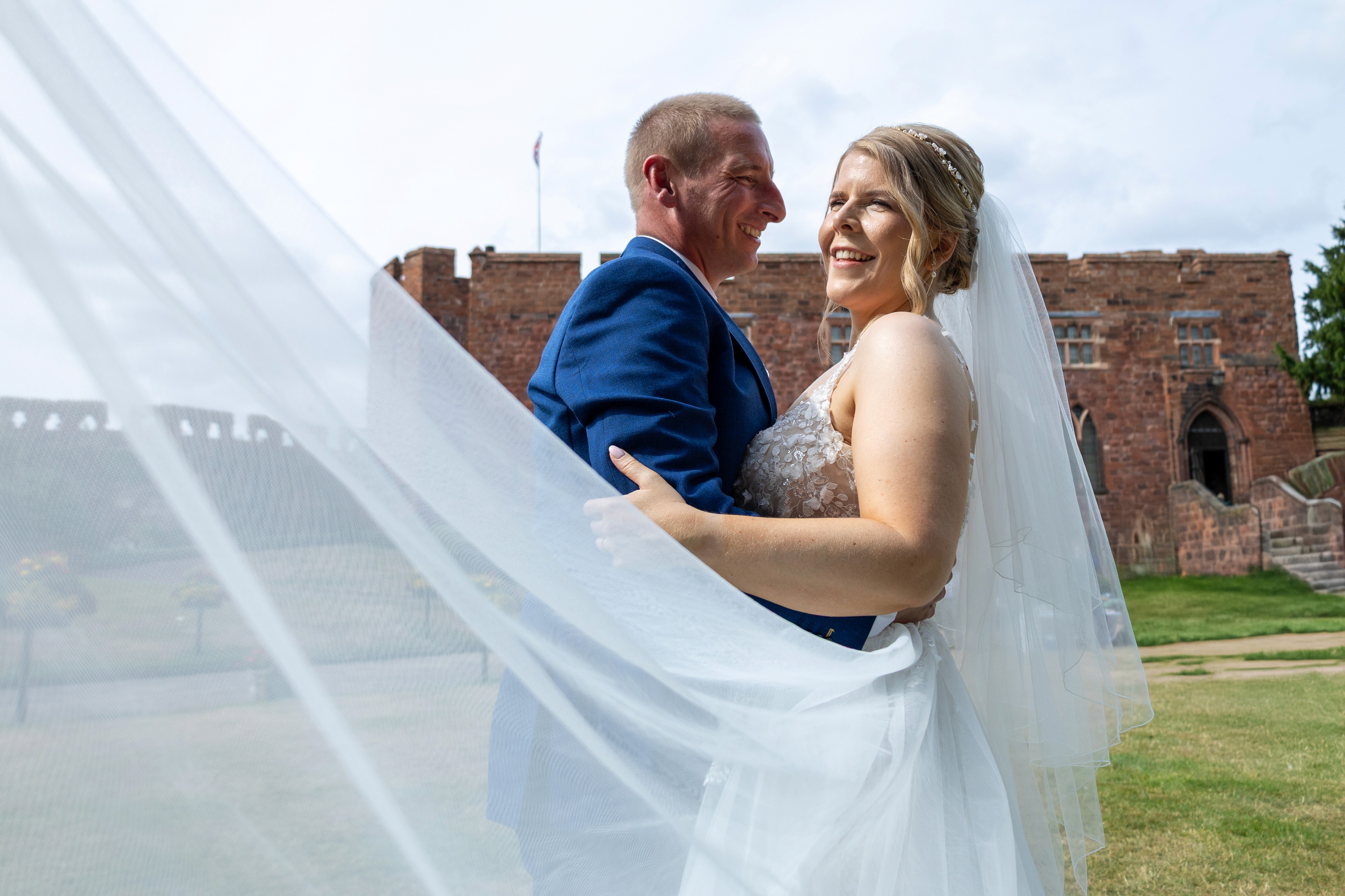 Will and Becs embracing with her veil flowing in front of Shrewsbury Castle