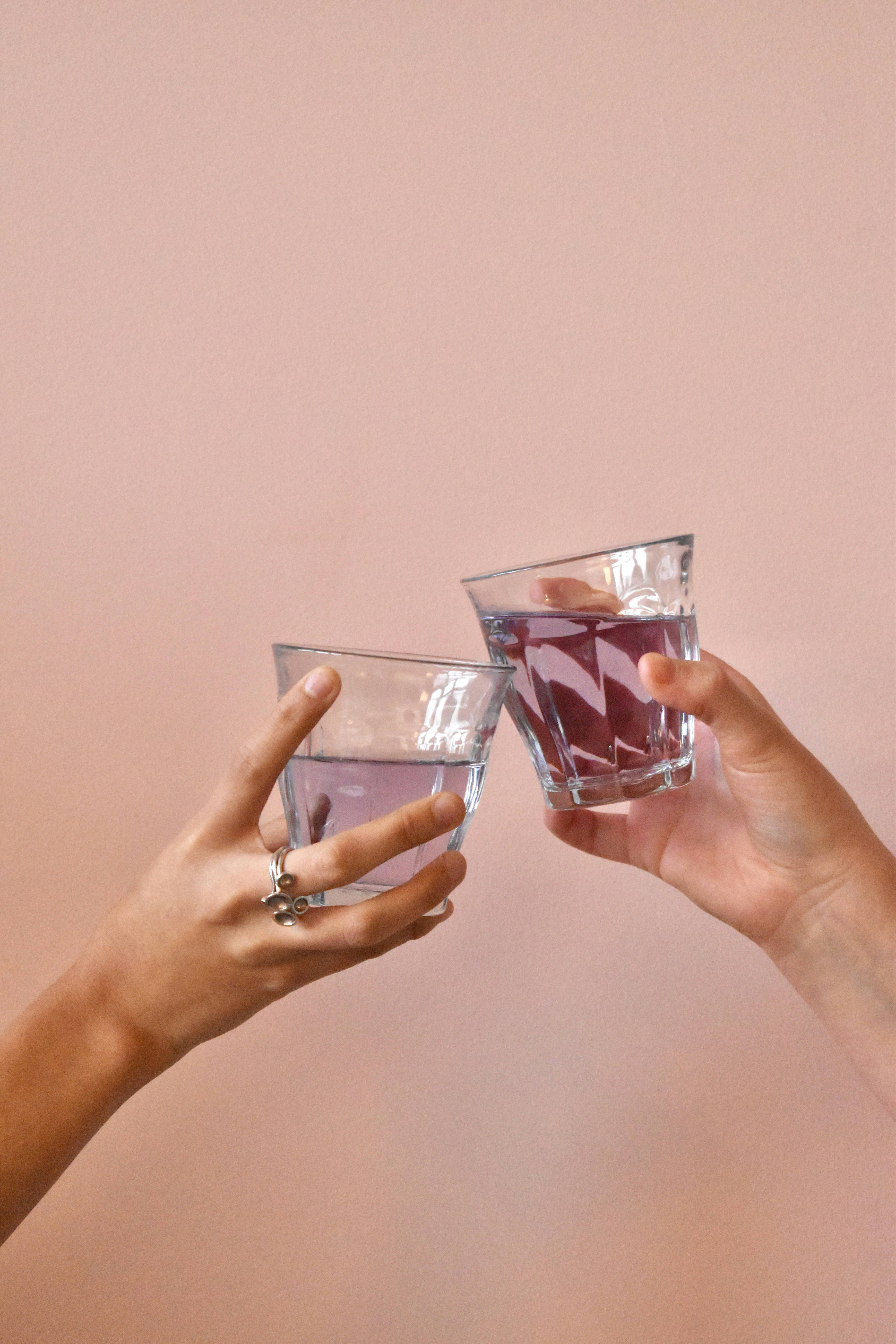 two hands holding glasses with liquid in them