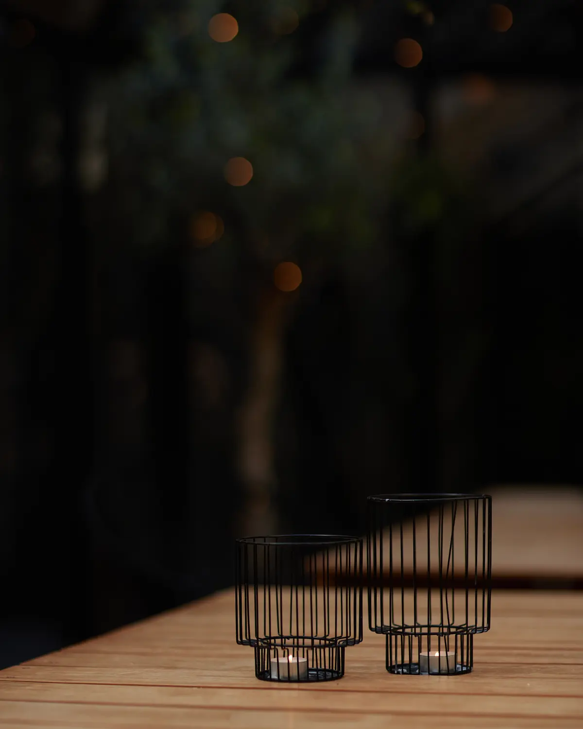 Black wire candle holders on a wooden table inside the courtyard greenhouse.