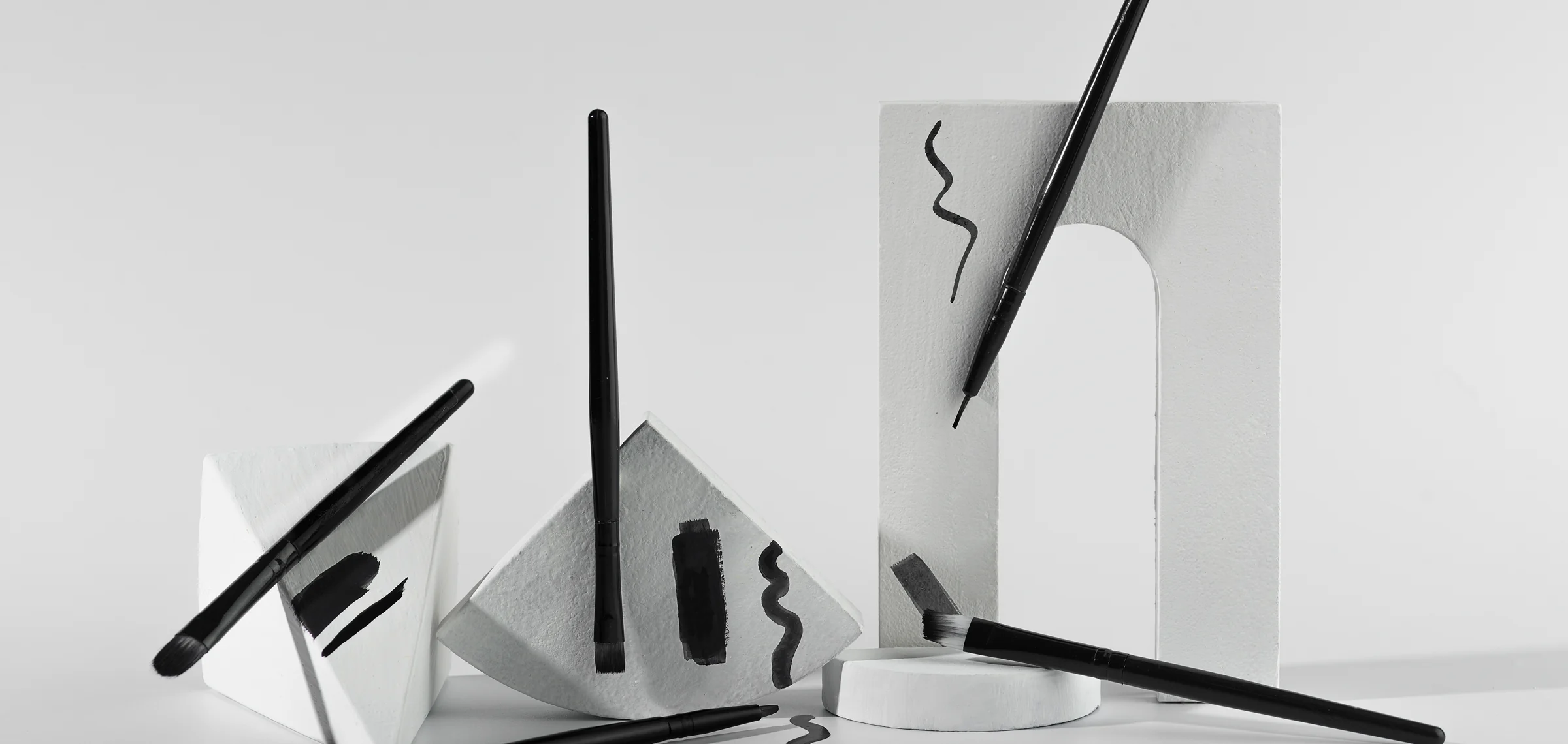 Минималистичная композиция с чёрными кистями и абстрактными мазками на белых геометрических формах