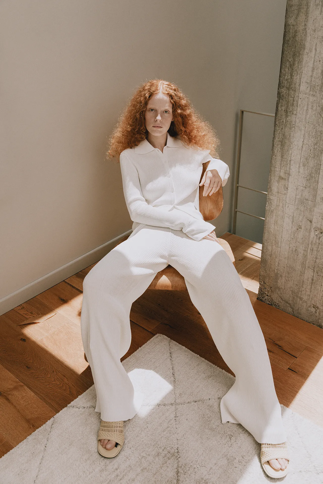 Annapurna SS26 collection white ribbed knit cardigan and trousers set worn by a seated model.