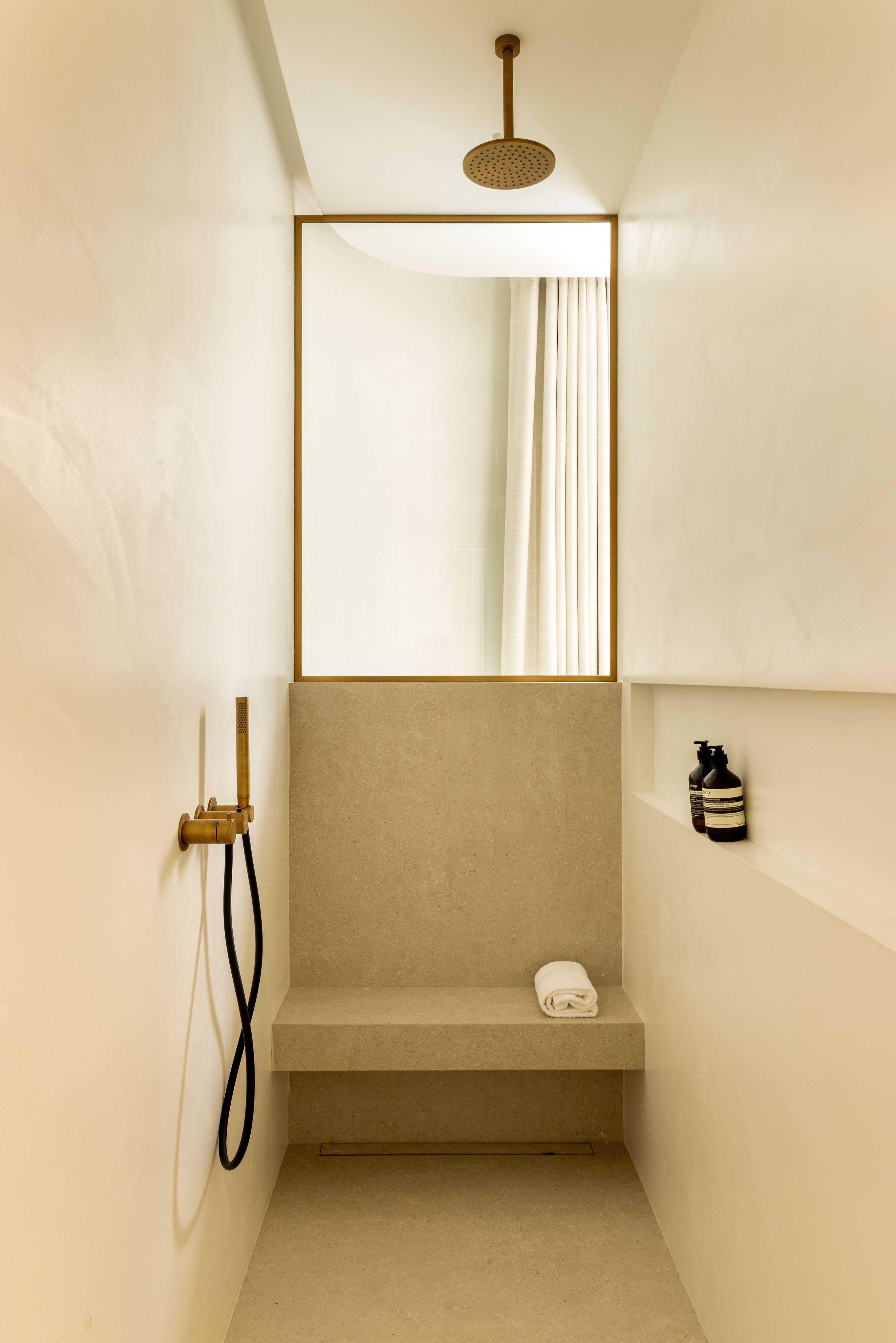 Douche italienne minimaliste avec banc en pierre, robinetterie doree et rideau de separation