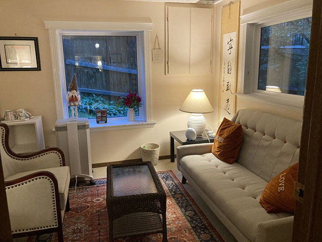 A photo of small cozy counselling office with 2 windows, 2 couches facing each other, and a coffee table