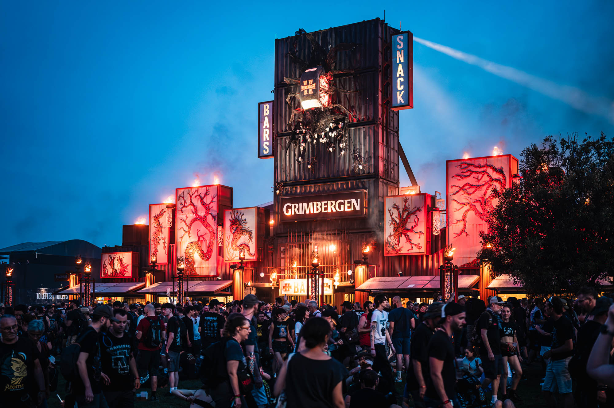Façade du bar et snack du festival illuminée en rouge et orange à la tombée de la nuit
