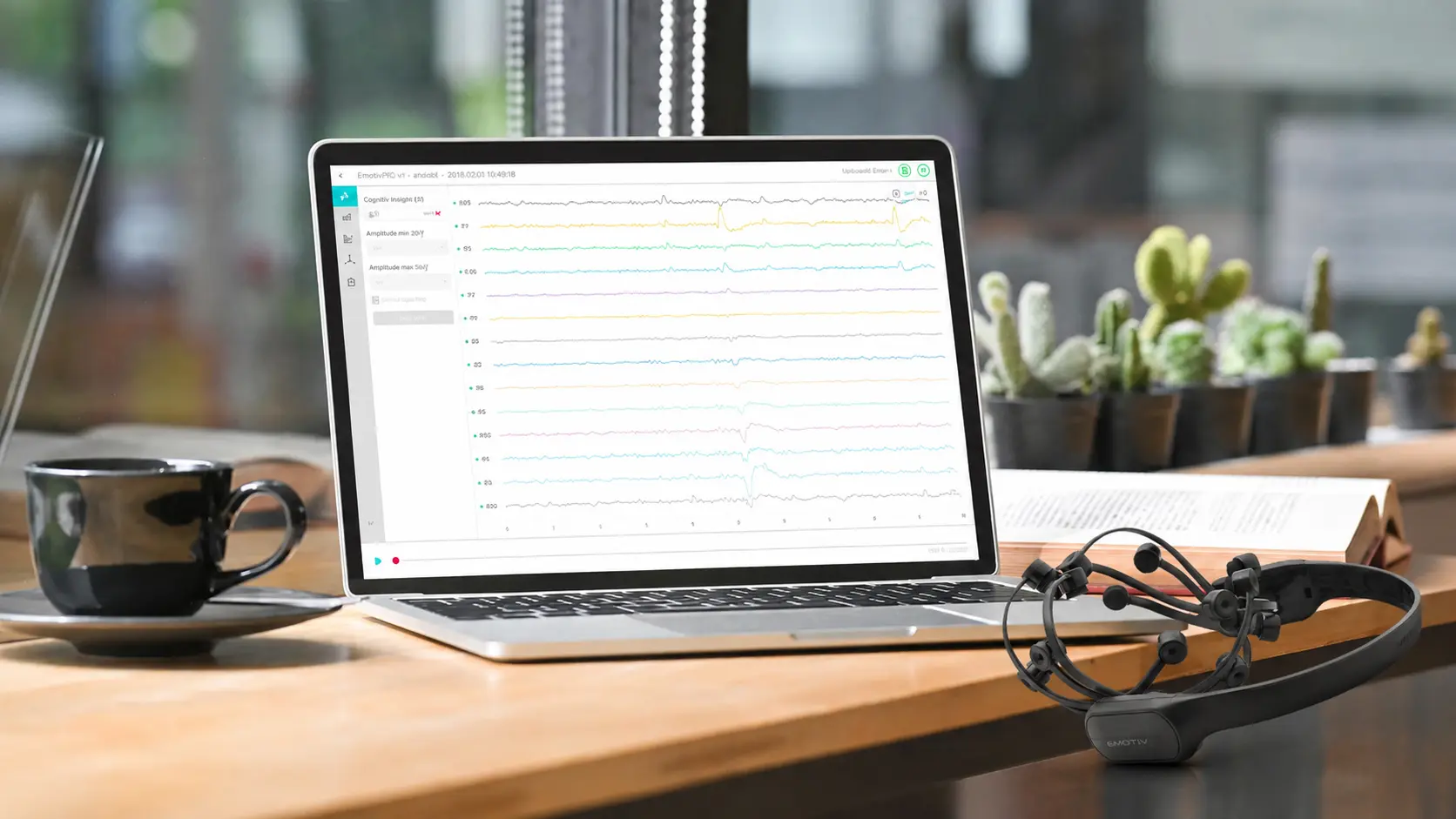 سماعة الرأس اللاسلكية Epoc EEG موضوعة بجانب كمبيوتر محمول يعرض برنامج تحليل موجات الدماغ، مما يوضح إعدادًا محمولاً لأبحاث وتجميع بيانات تخطيط أمواج الدماغ في مجالات علم الأعصاب، و BCI، والدراسات الإدراكية.