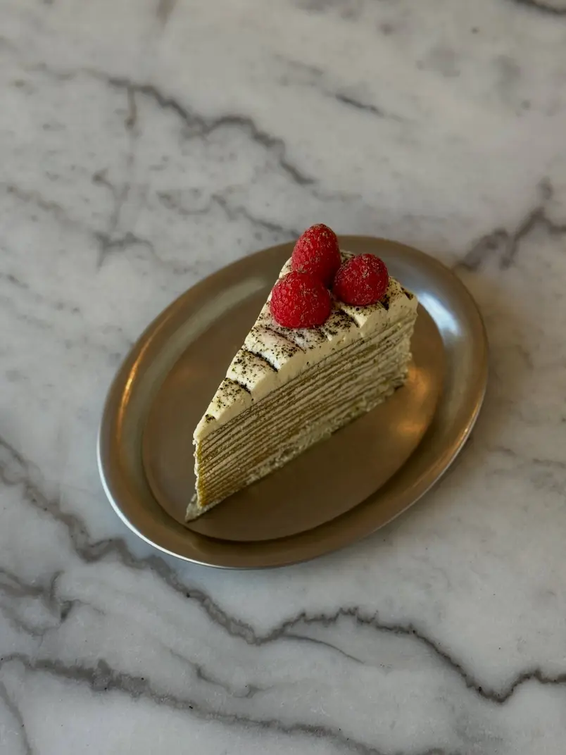A slice of matcha (green tea) layered cake topped with fresh raspberries, served on a gold-rimmed plate against a marble surface